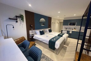 Una habitación de hotel moderna con dos camas, un kitchenette, una zona de estar y un espejo grande.