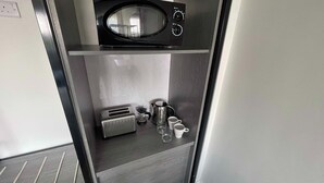 Eine kleine Küchenzeile mit Mikrowelle, Toaster, Wasserkocher und zwei Tassen auf einem Regal.