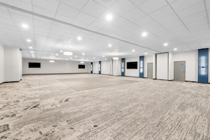 Una habitación amplia con piso alfombrado, paredes blancas y una serie de luces en el techo.