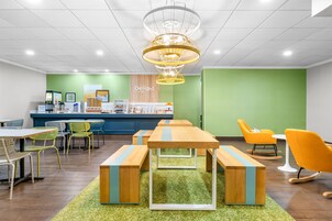 Un interior moderno con mesas y bancos de madera, paredes verdes y una zona de recepción.