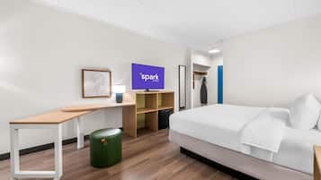A modern hotel room with a bed, desk, chair, TV, and storage shelves.