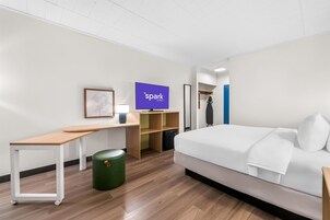 Quarto de hotel moderno com cama, escrivaninha, cadeira, televisão e estantes.