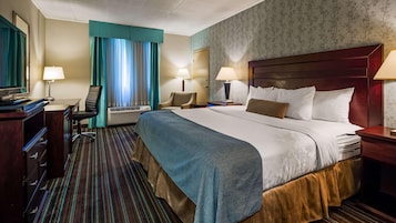 Una habitación de hotel con cama, escritorio, silla, televisión y ventana con cortinas.