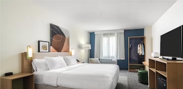 Habitación de hotel con cama, mesitas de noche, televisor, armario y ventana con cortinas.