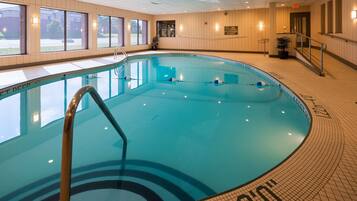 En indendørs swimmingpool med krystalklart vand, et springbræt og et skilt for livredder.