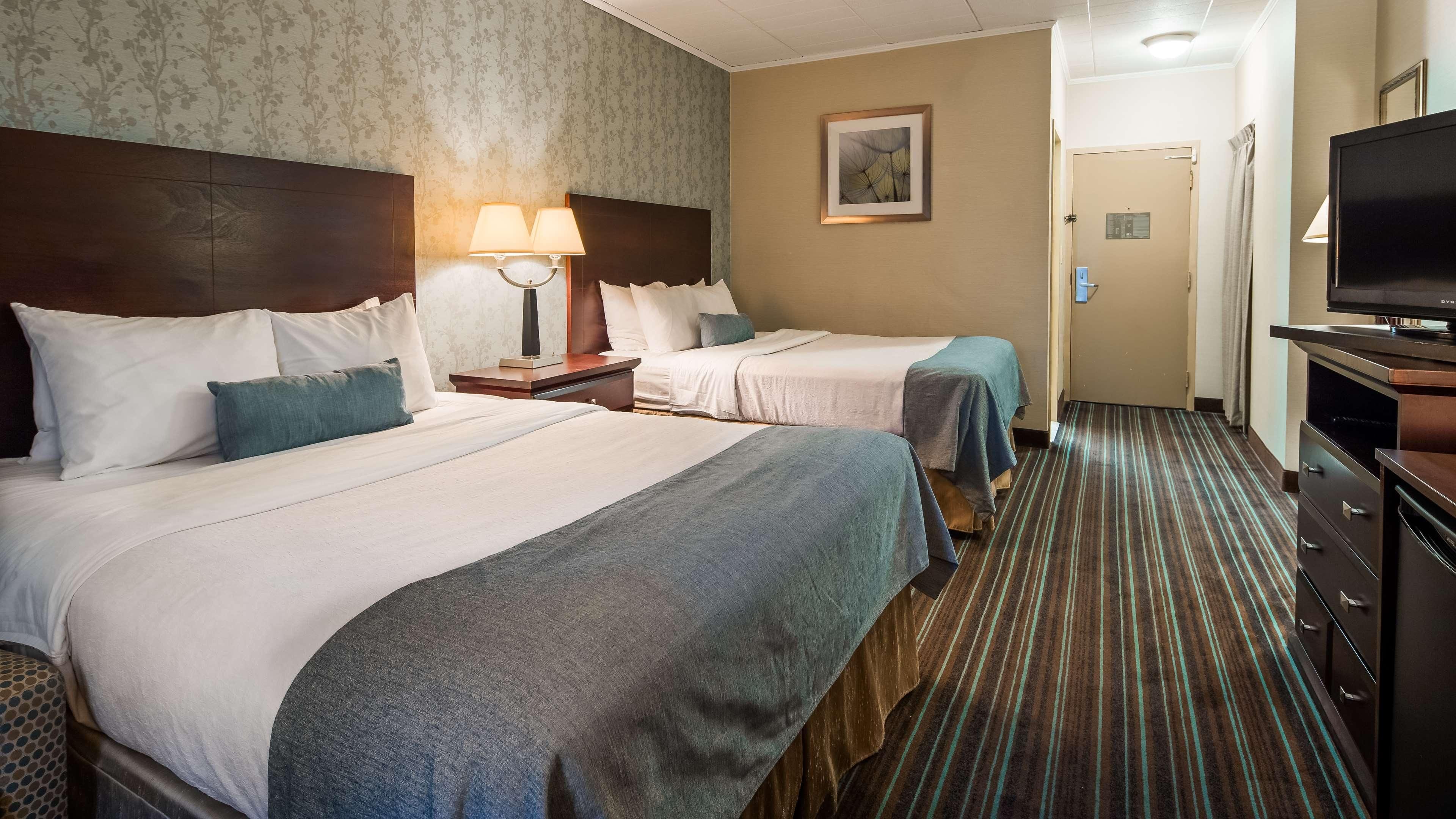 A hotel room with two beds, a TV, a lamp, and a door leading to another room.