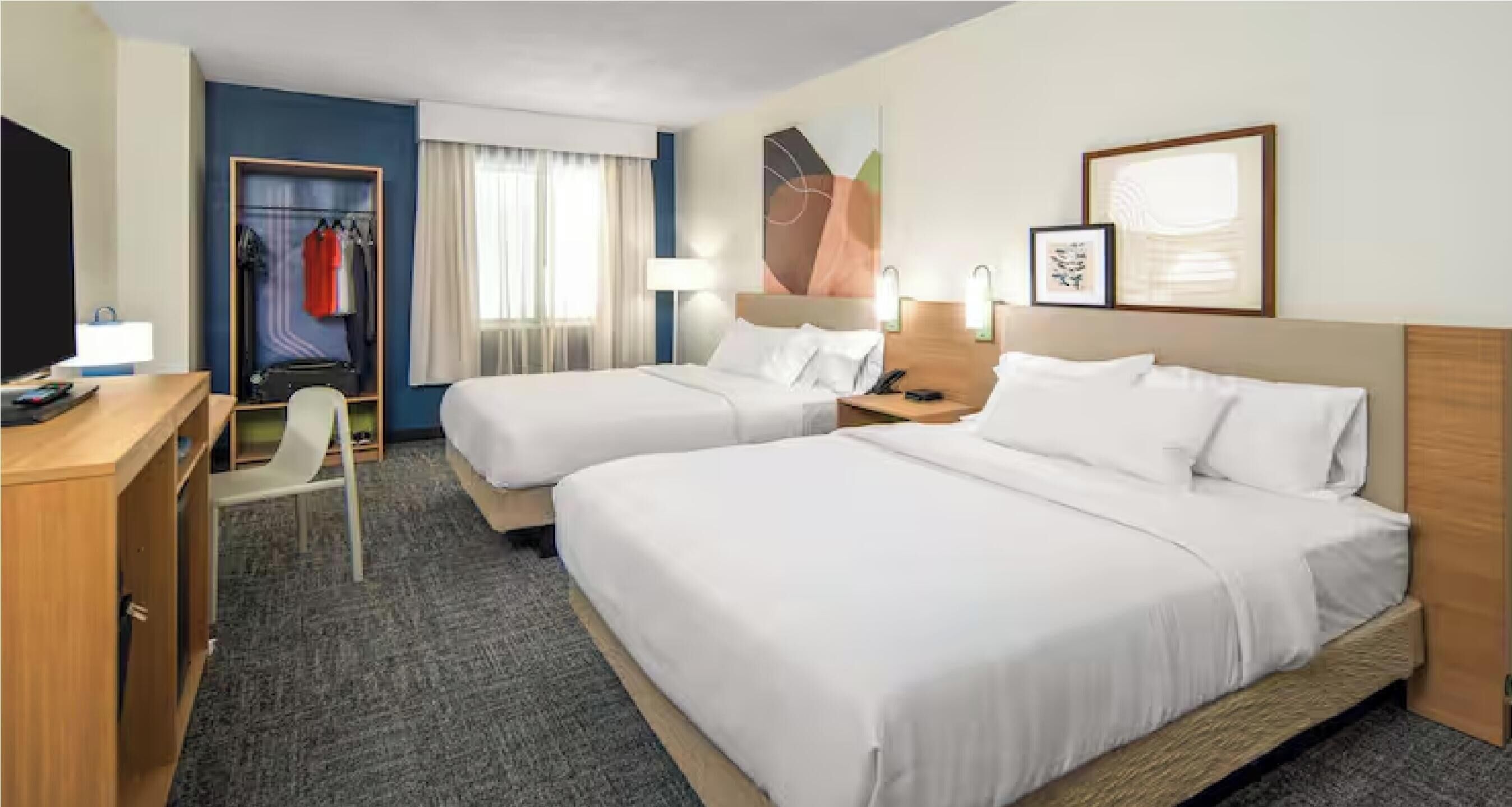 Habitación de hotel con dos camas, un escritorio, una silla, un armario y baño.