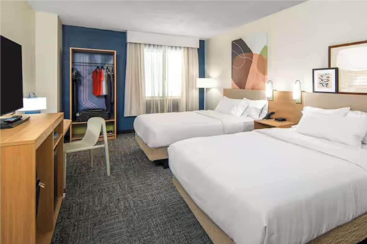 Une chambre d’hôtel avec deux lits, un bureau, une chaise, une armoire et une salle de bain.