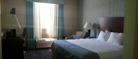 A hotel room with a bed, a chair, a desk, and a lamp.