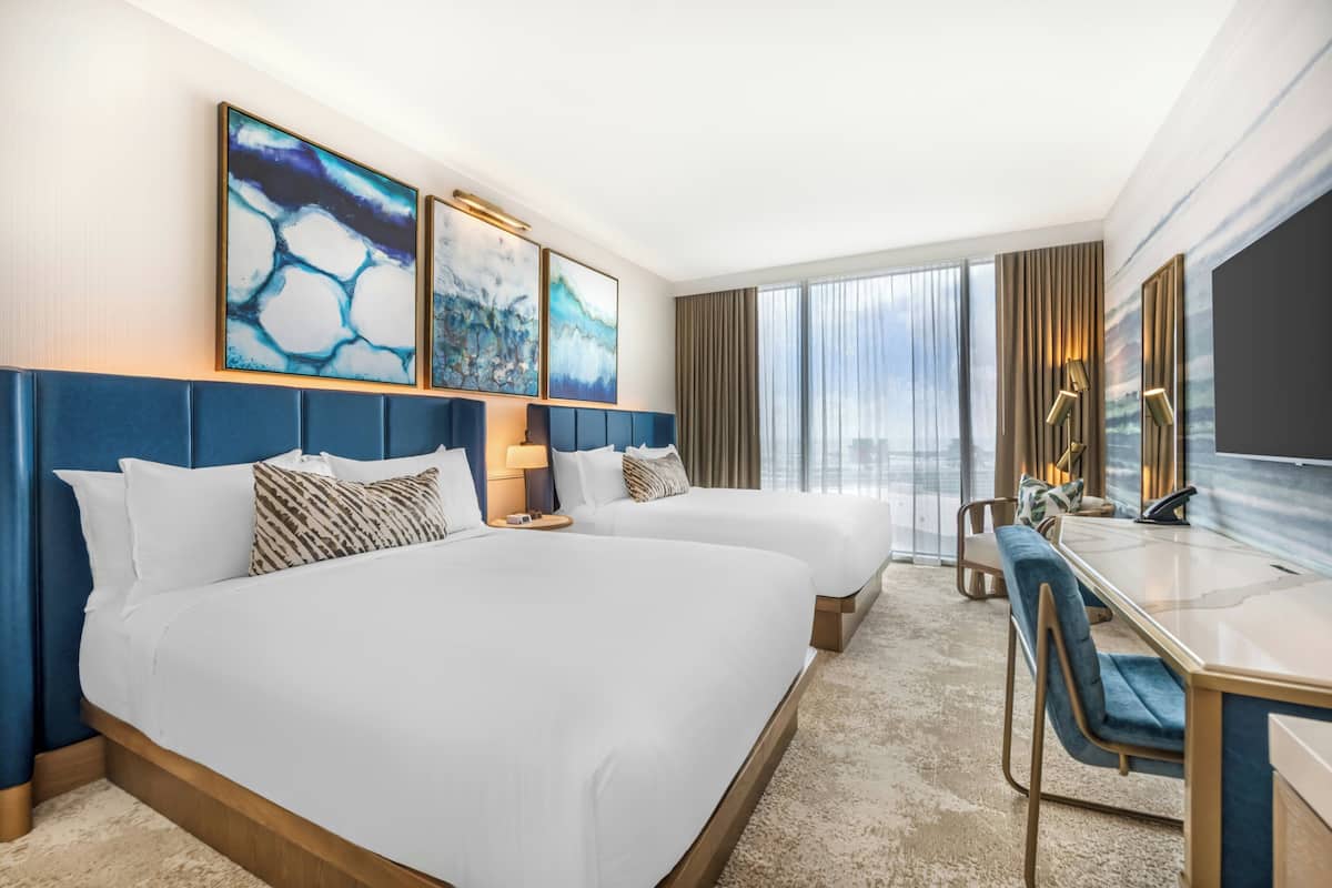 Une chambre d’hôtel avec deux lits, un bureau et une grande fenêtre.