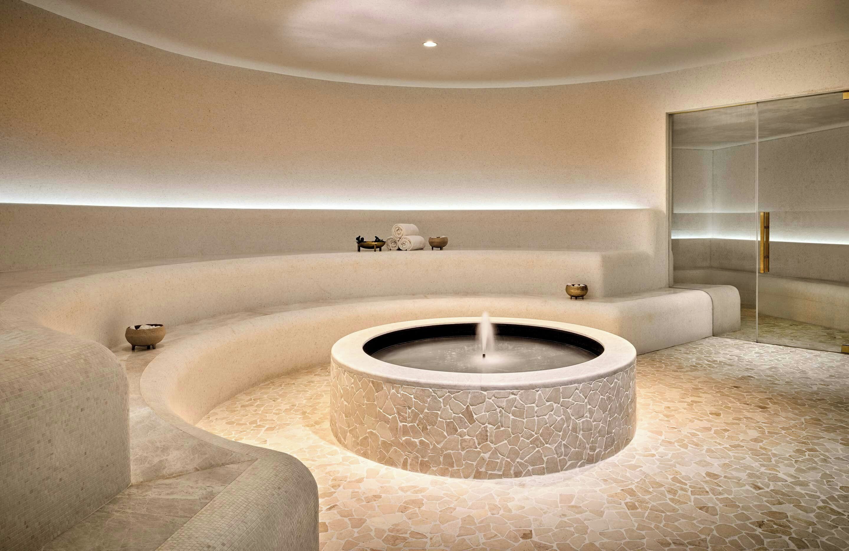 A spa area with a circular hot tub, seating, and a stone floor.