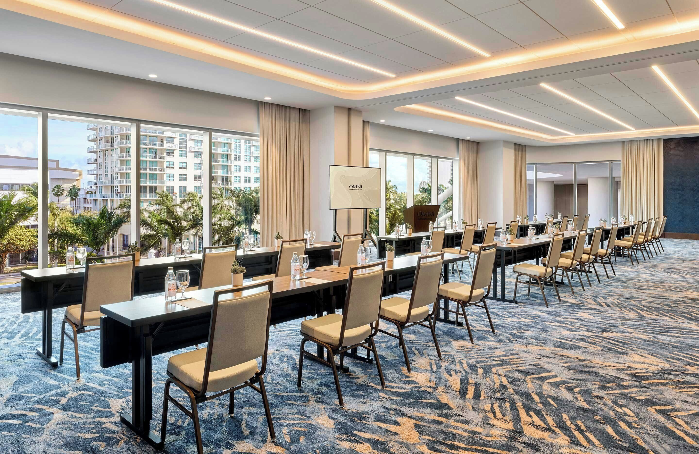 Un salón de conferencias con largas mesas, sillas y un ventanal con vistas a la ciudad.