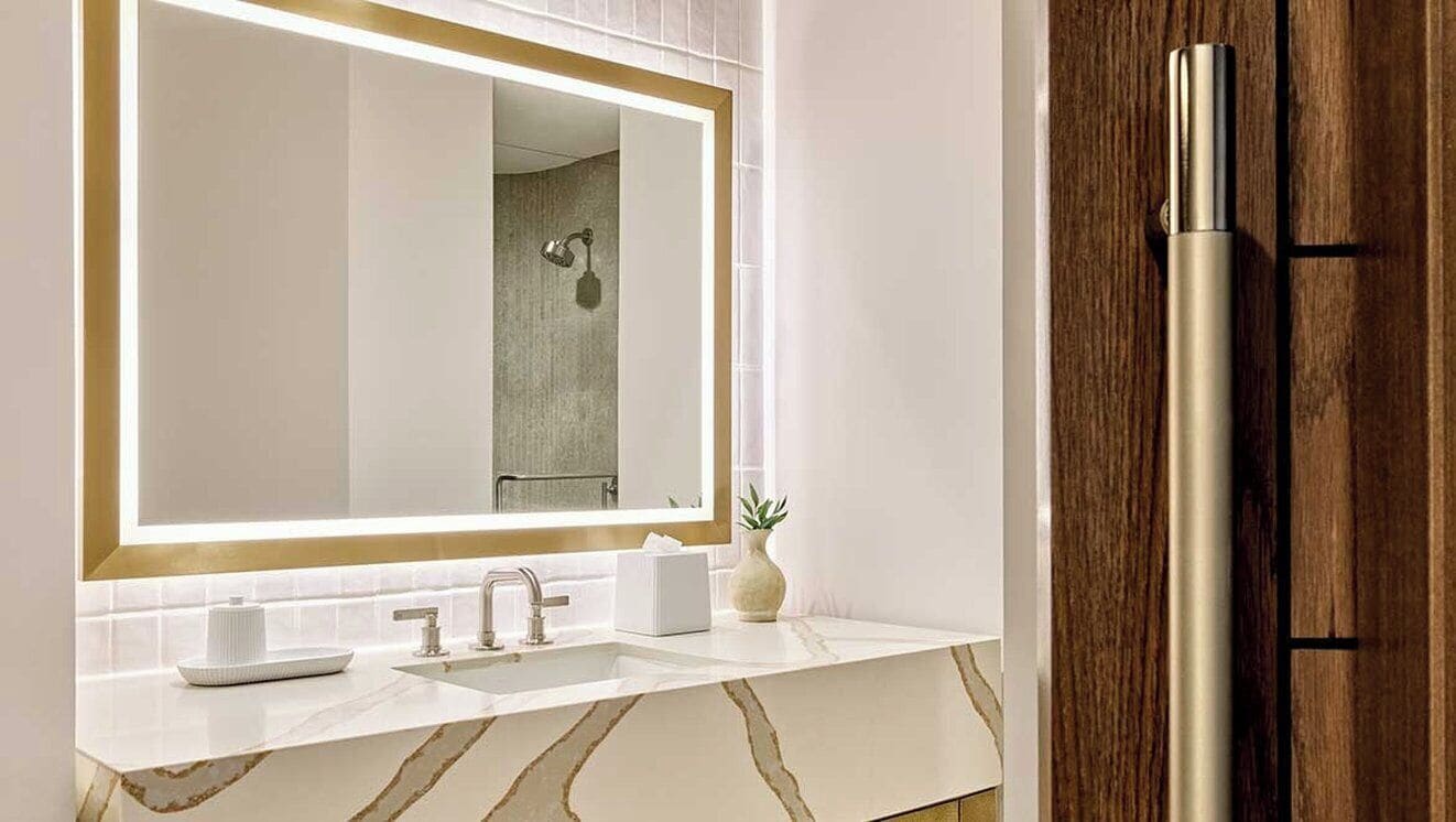 Une salle de bain avec un grand miroir, un lavabo, un porte-serviettes et une porte en bois.