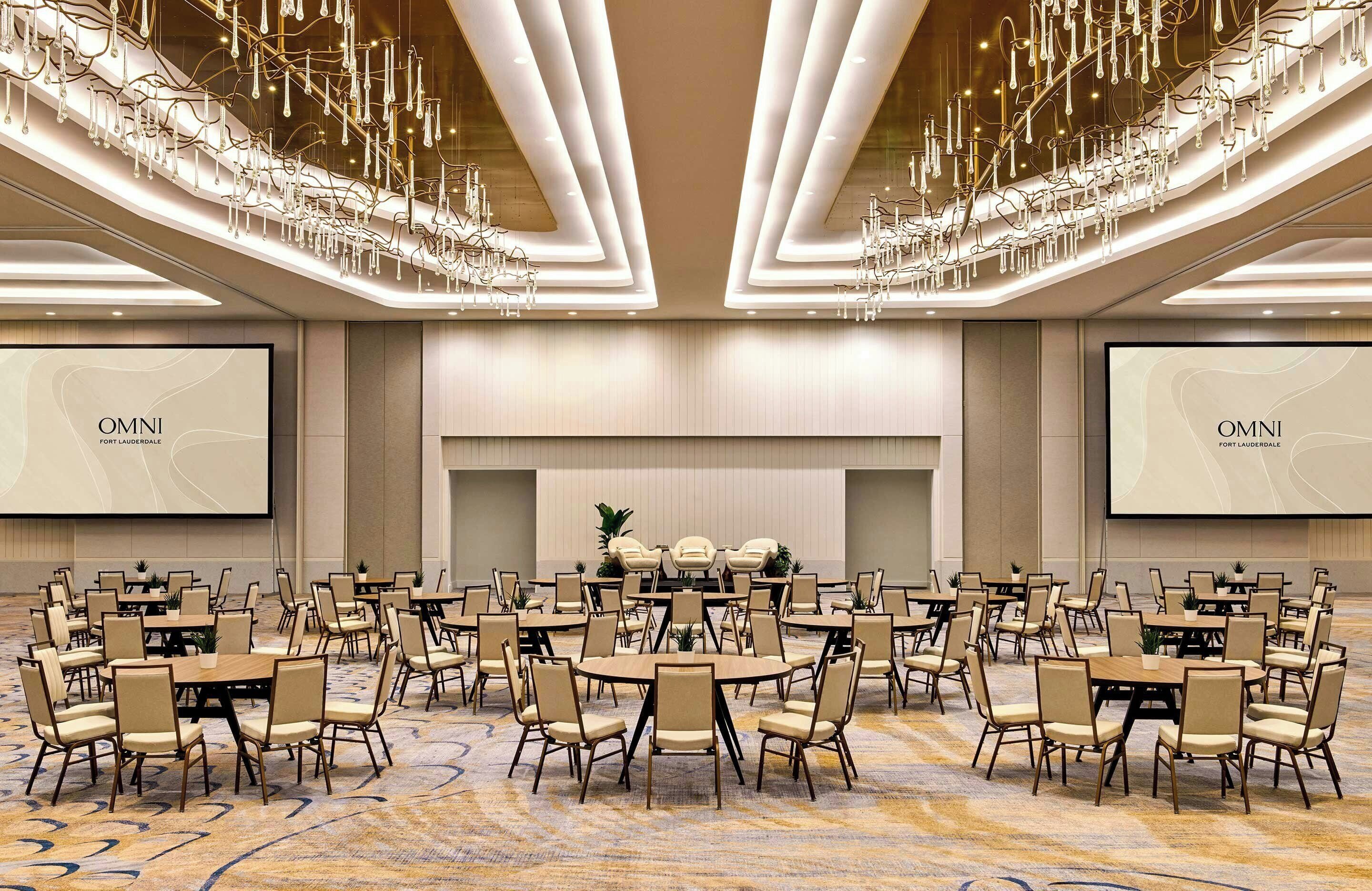 A conference room with round tables and chairs, a large screen, and a chandelier.