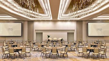 A conference room with round tables and chairs, a large screen, and a chandelier.