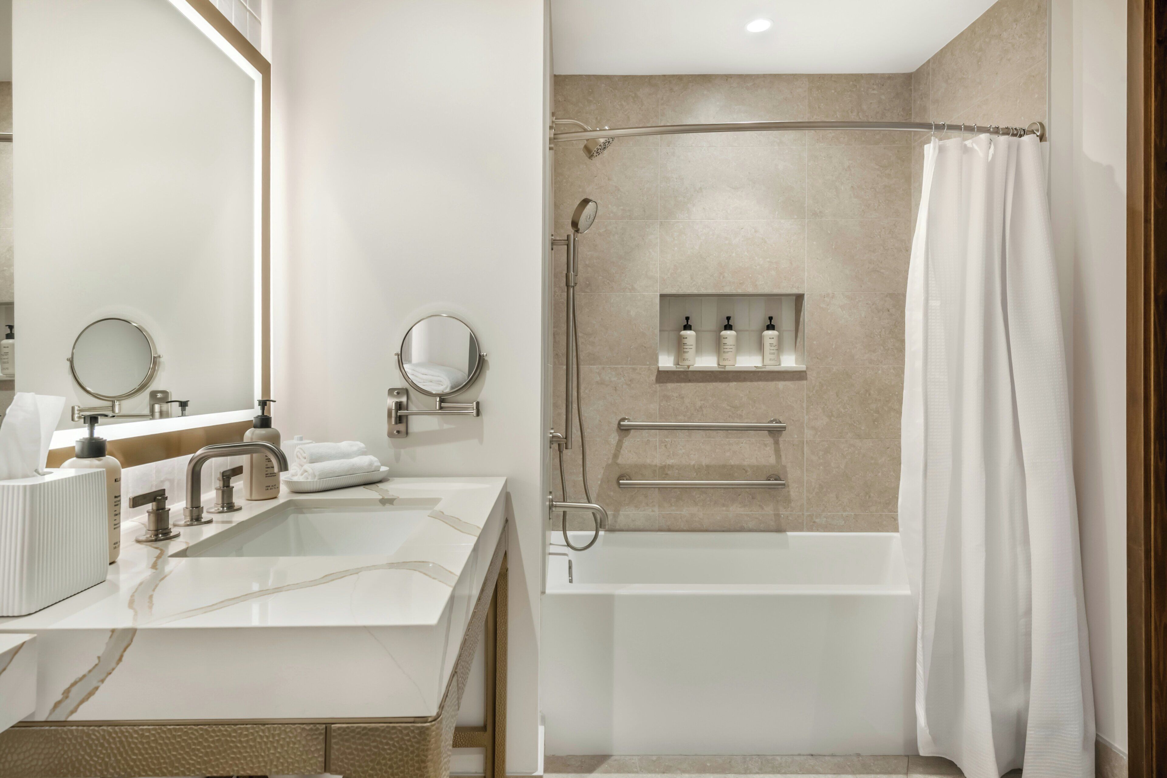 A modern bathroom with a double sink, two mirrors, a bathtub, and a shower.