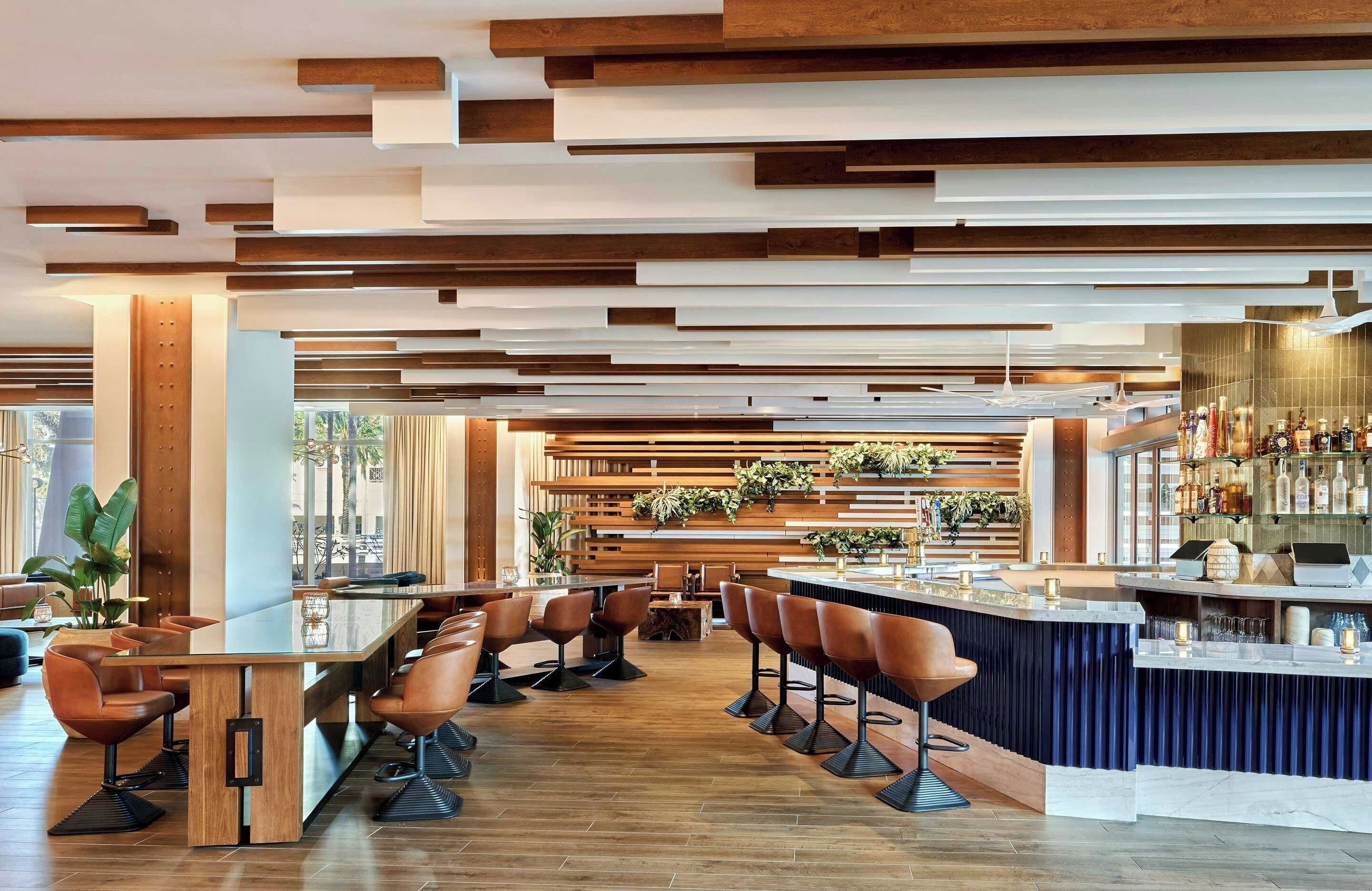 Un bar moderno con una barra larga, varios taburetes y un diseño de techo de madera.