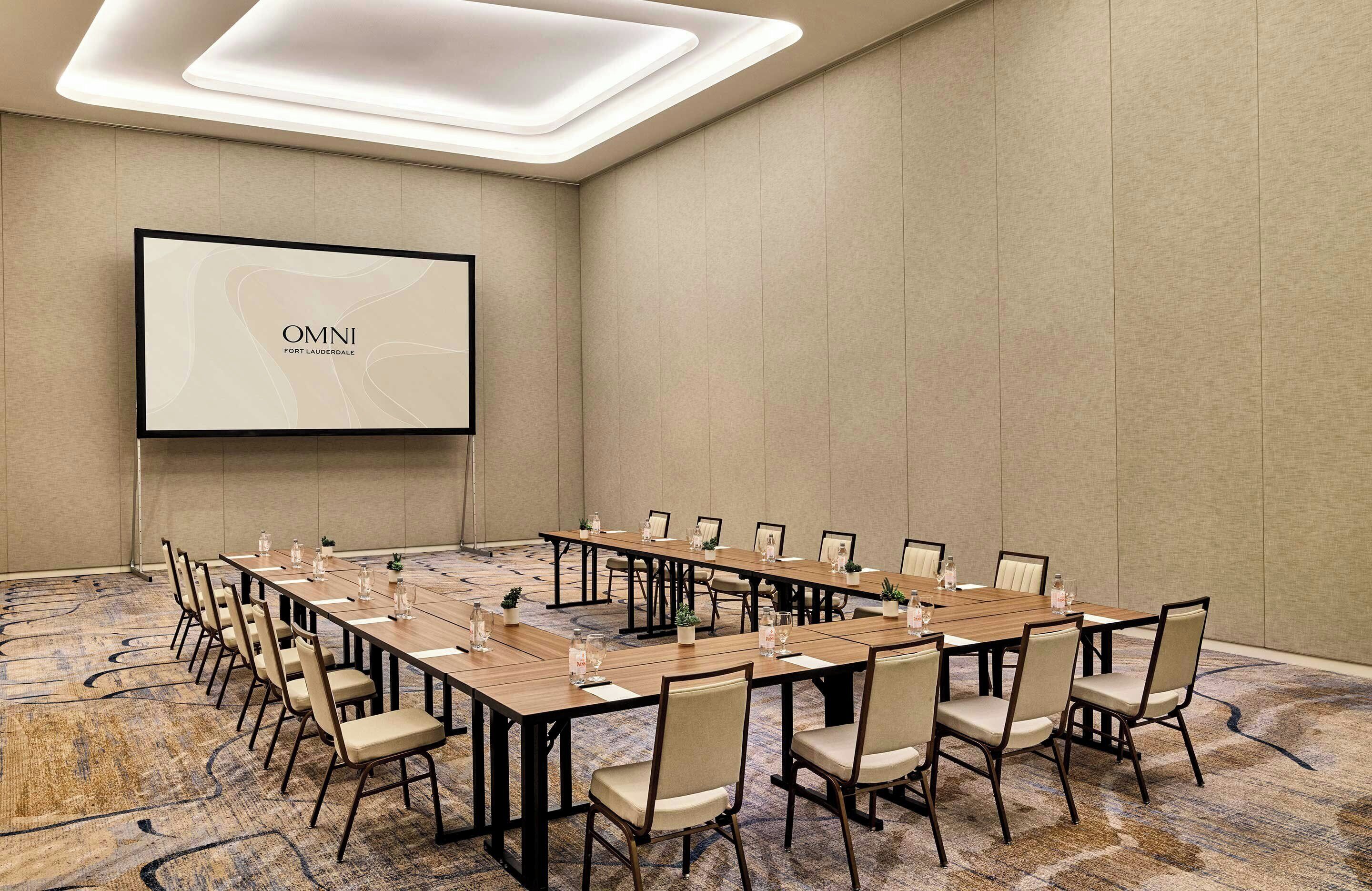 Ein Konferenzraum mit langem Tisch, Stühlen, einer Projektionsleinwand und Teppichboden.
