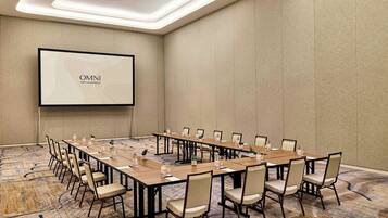 Ein Konferenzraum mit langem Tisch, Stühlen, einer Projektionsleinwand und Teppichboden.