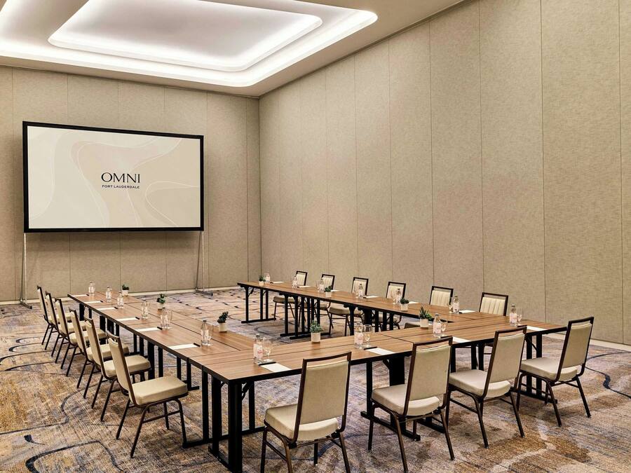 Ein Konferenzraum mit langem Tisch, Stühlen, einer Projektionsleinwand und Teppichboden.