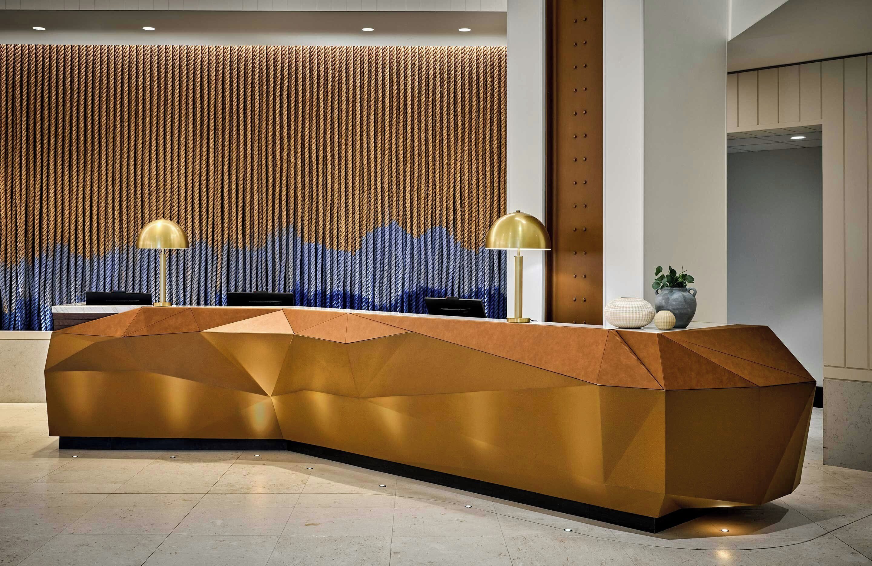 A reception desk with a geometric design, a vertical textured wall, and a lamp.