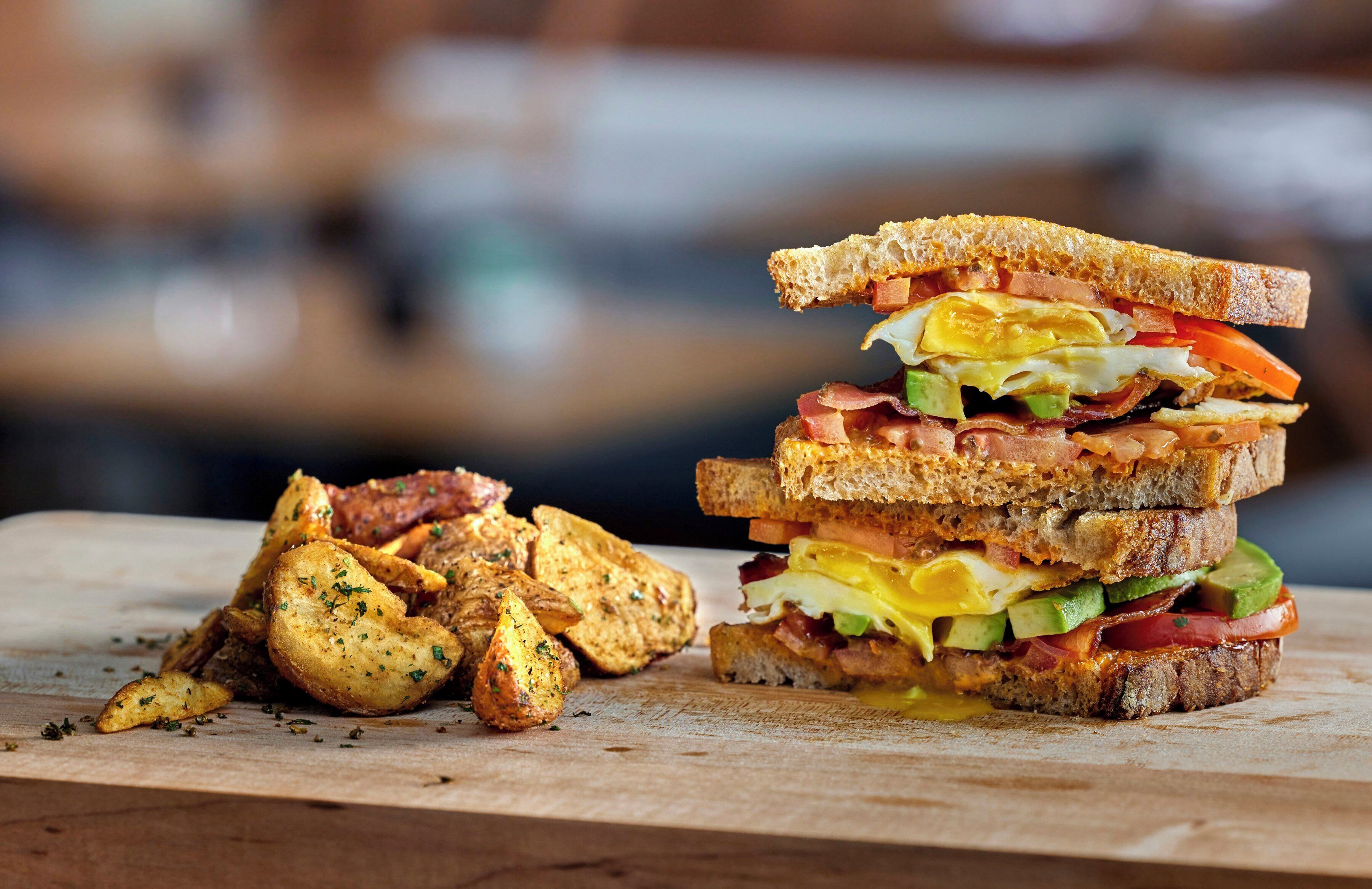 A sandwich with multiple layers of ingredients, accompanied by a side of seasoned potato wedges on a wooden surface.