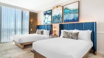 A hotel room with two beds, a large window with curtains, and three abstract paintings on the wall.