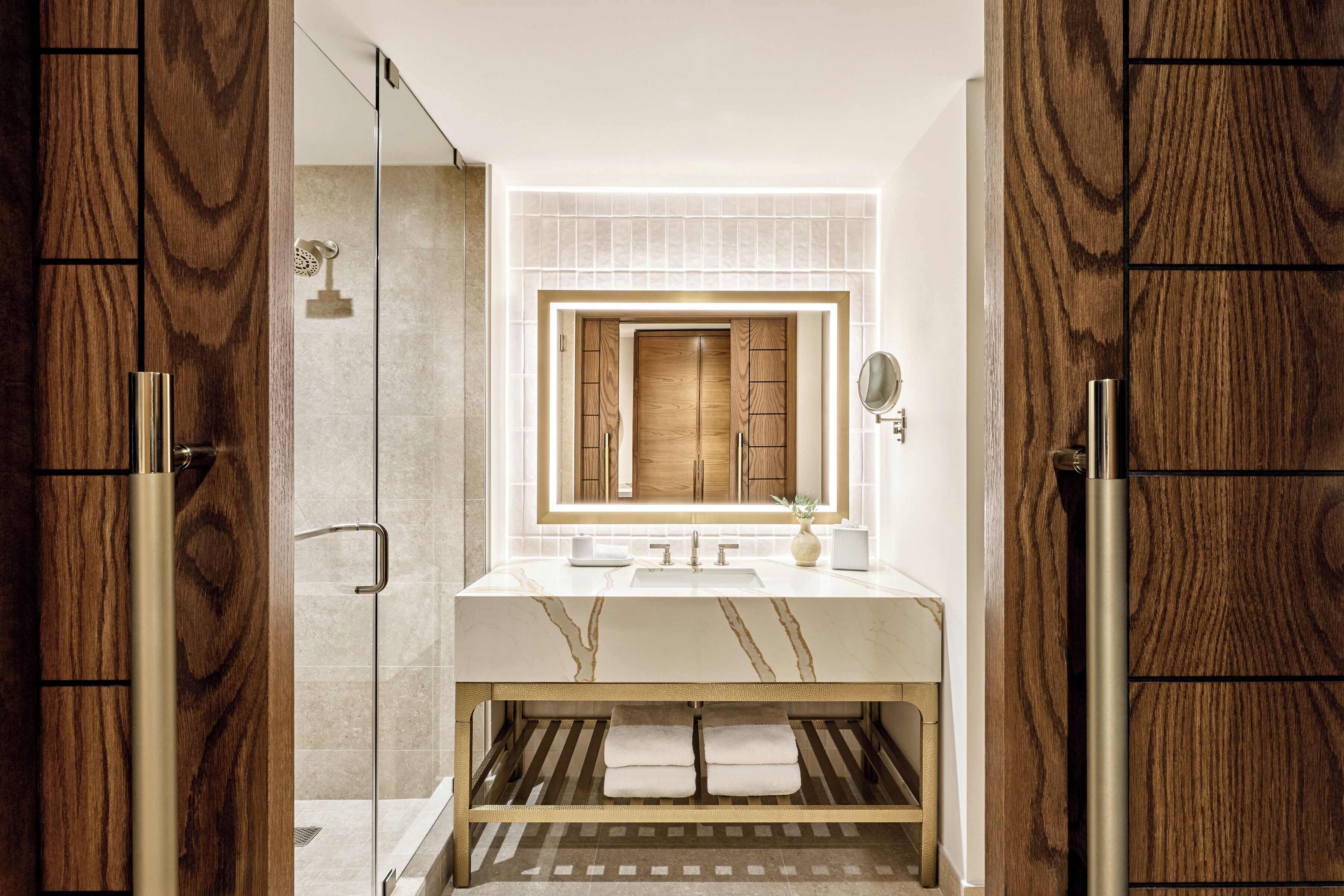 A modern bathroom with a wooden vanity, a glass shower enclosure, and a marble sink.