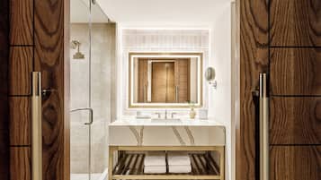 A modern bathroom with a wooden vanity, a glass shower enclosure, and a marble sink.