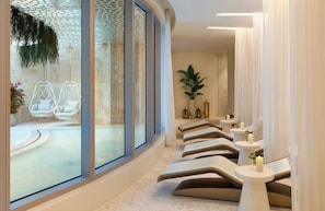 Ein Wellnessbereich mit großem Fenster, einer Sitzgelegenheit mit Kissen und einer Wandpflanze.
