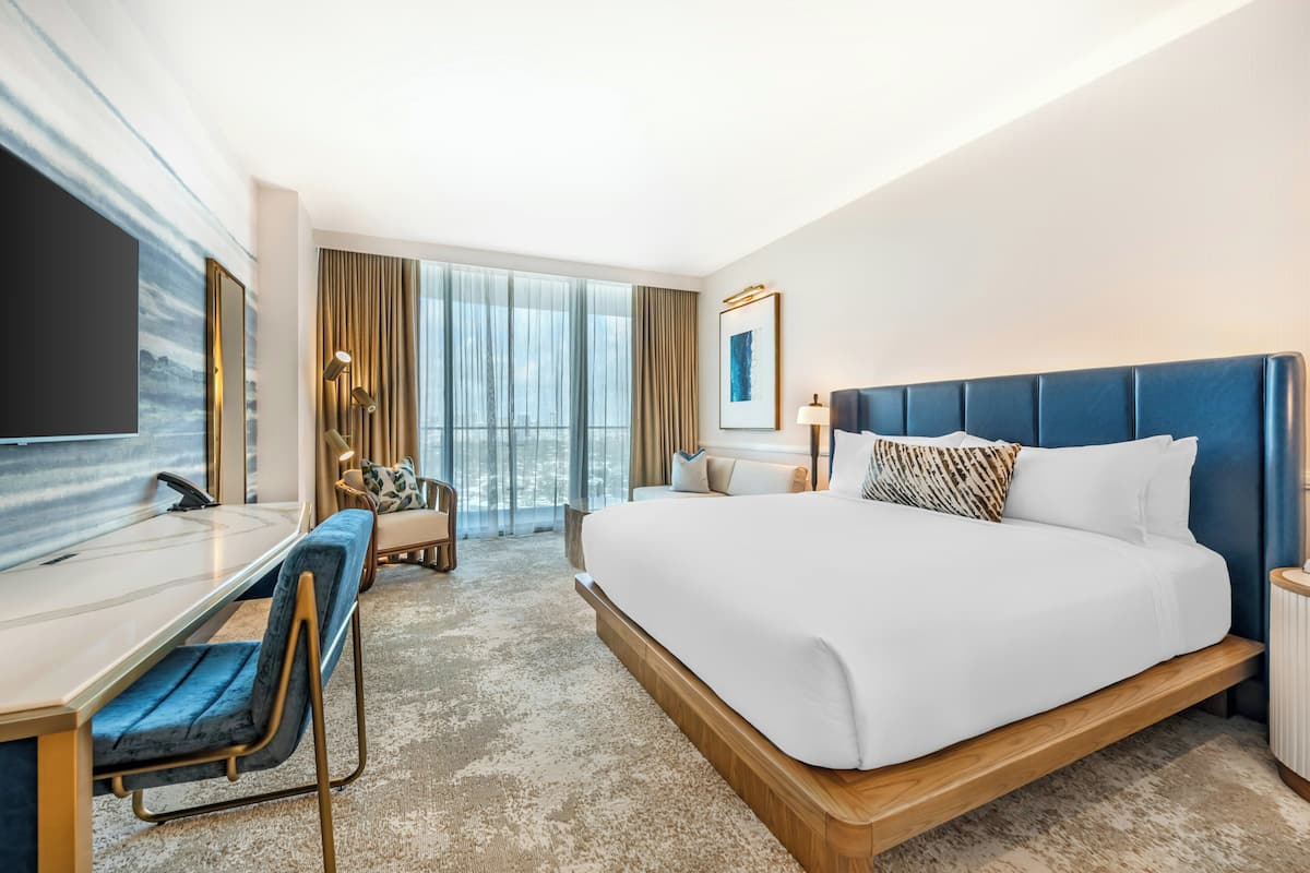 Une chambre d’hôtel moderne dotée d’un grand lit, d’un bureau, d’une chaise, d’une télévision et d’une grande fenêtre avec des rideaux.