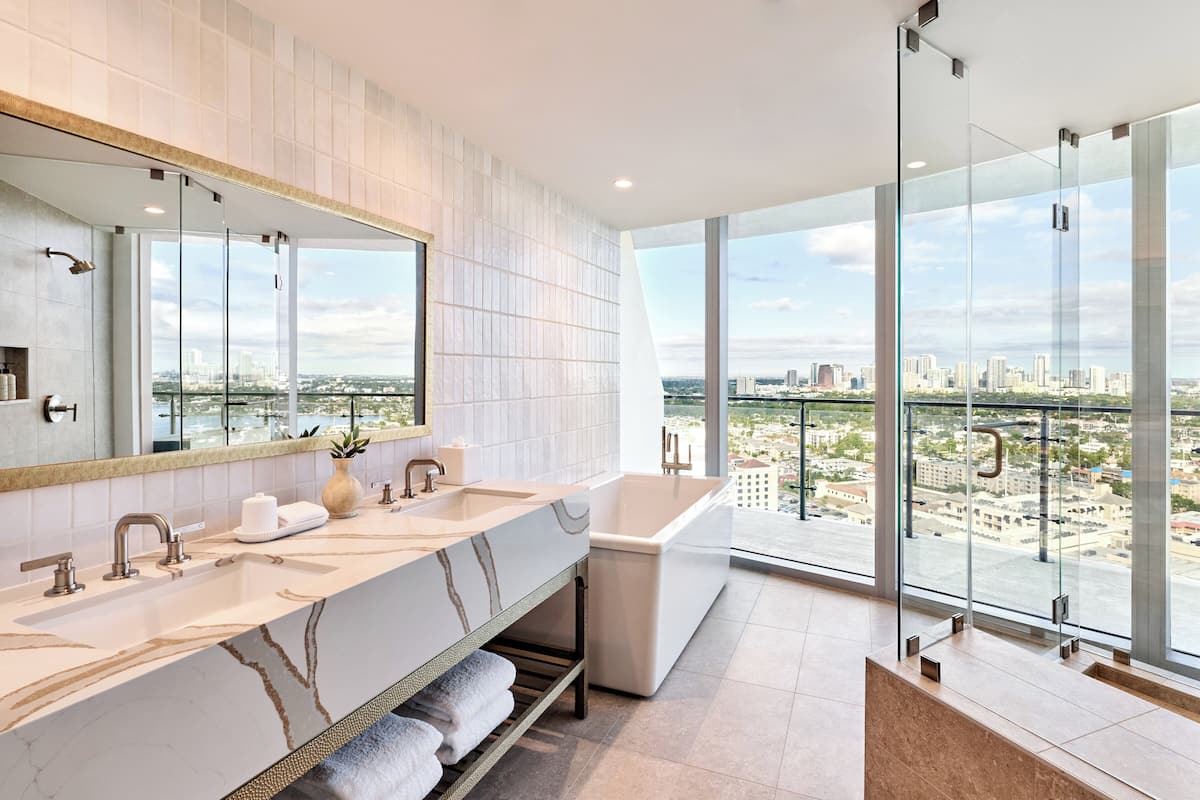 Une salle de bain moderne avec un grand miroir, deux lavabos, une baignoire et une douche à l’italienne.