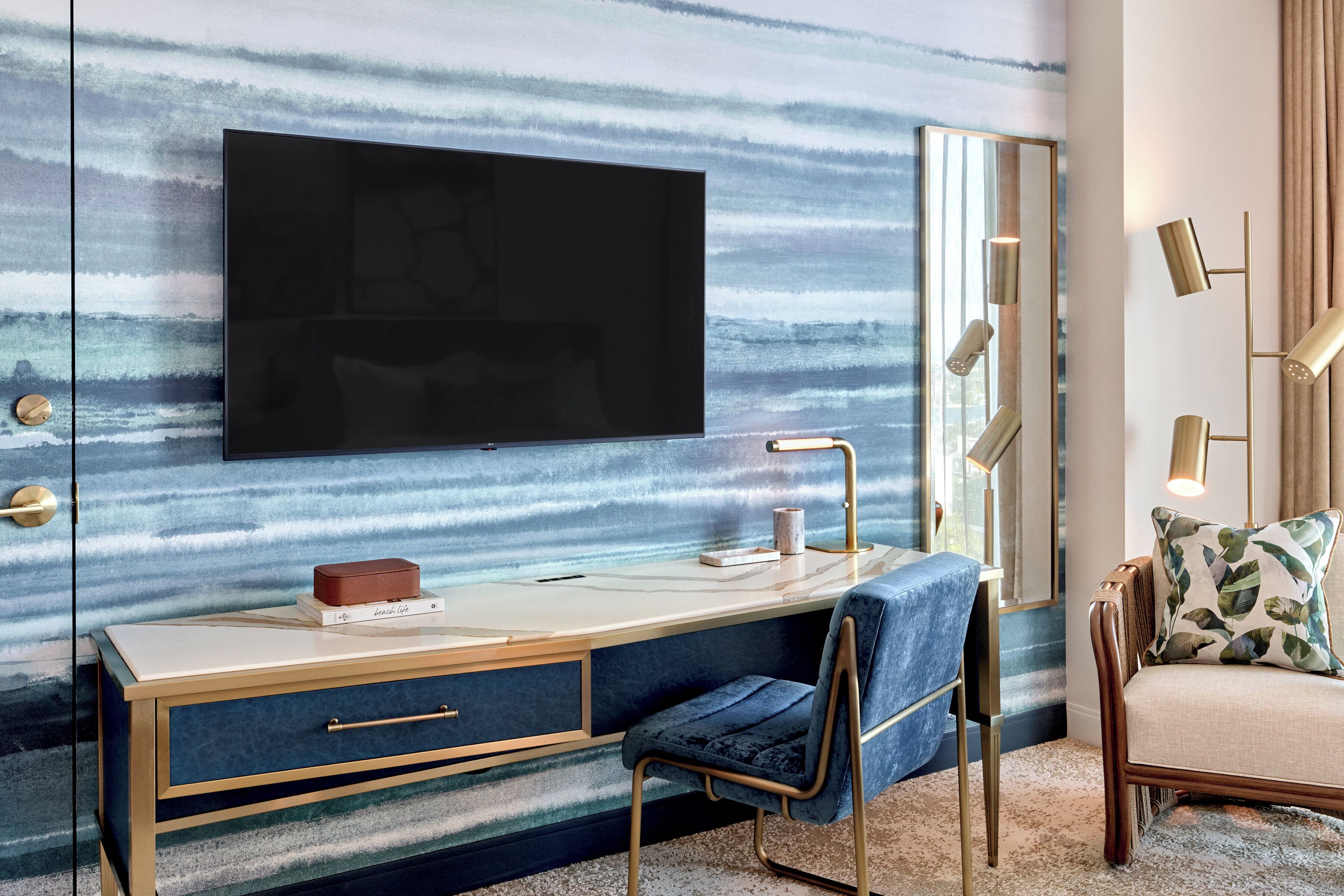 Un dormitorio moderno con una televisión de pantalla plana grande montada en una pared texturizada, una mesita de noche con una lámpara, una silla y un espejo grande.