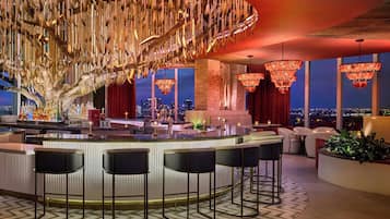 Un área de bar moderna con una barra central, taburetes y vistas de la ciudad a través de amplios ventanales.