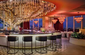 Un área de bar moderna con una barra central, taburetes y vistas de la ciudad a través de amplios ventanales.