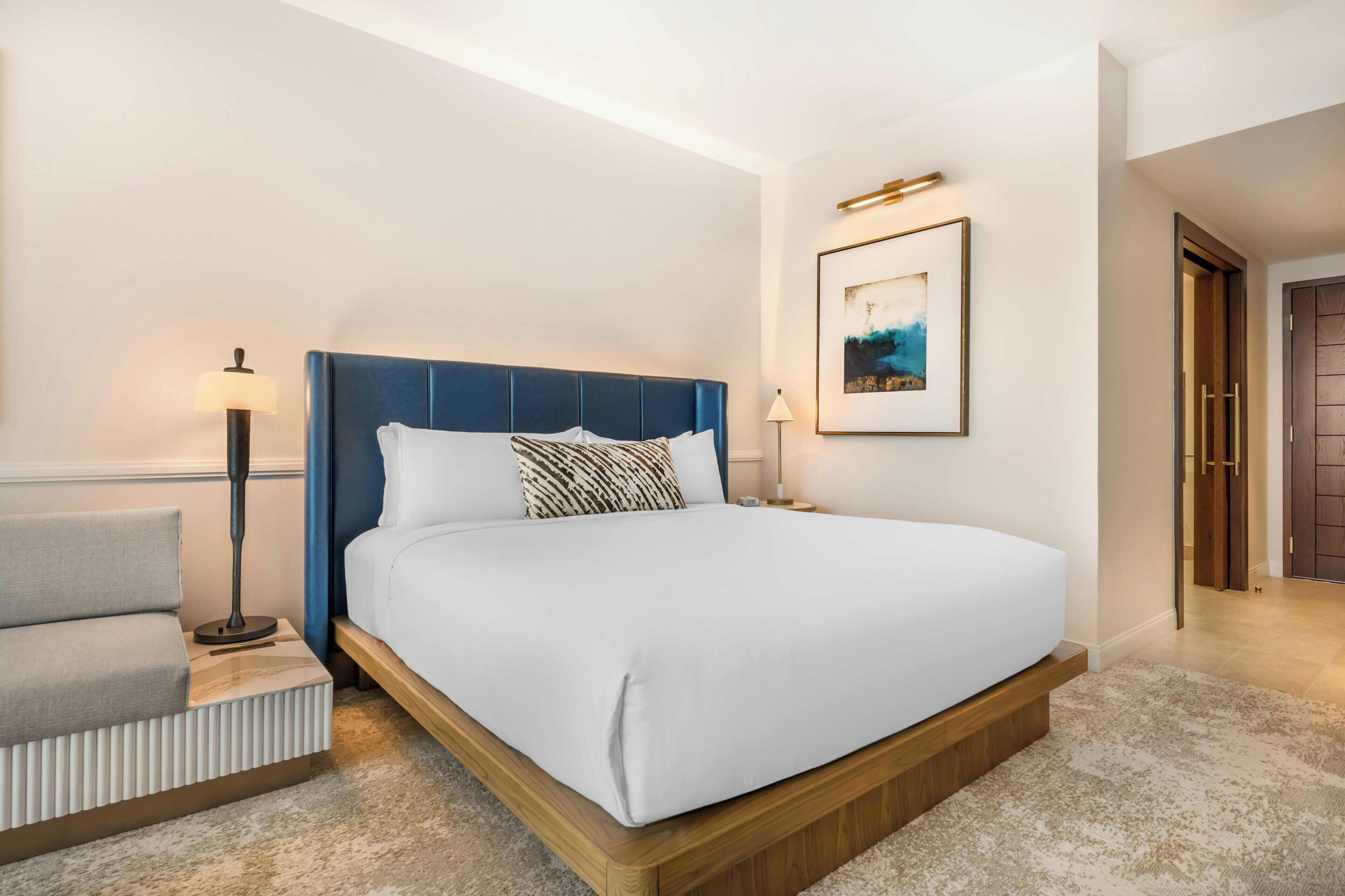 Une chambre d’hôtel avec un lit, une table de chevet, une lampe et un tableau encadré au mur.