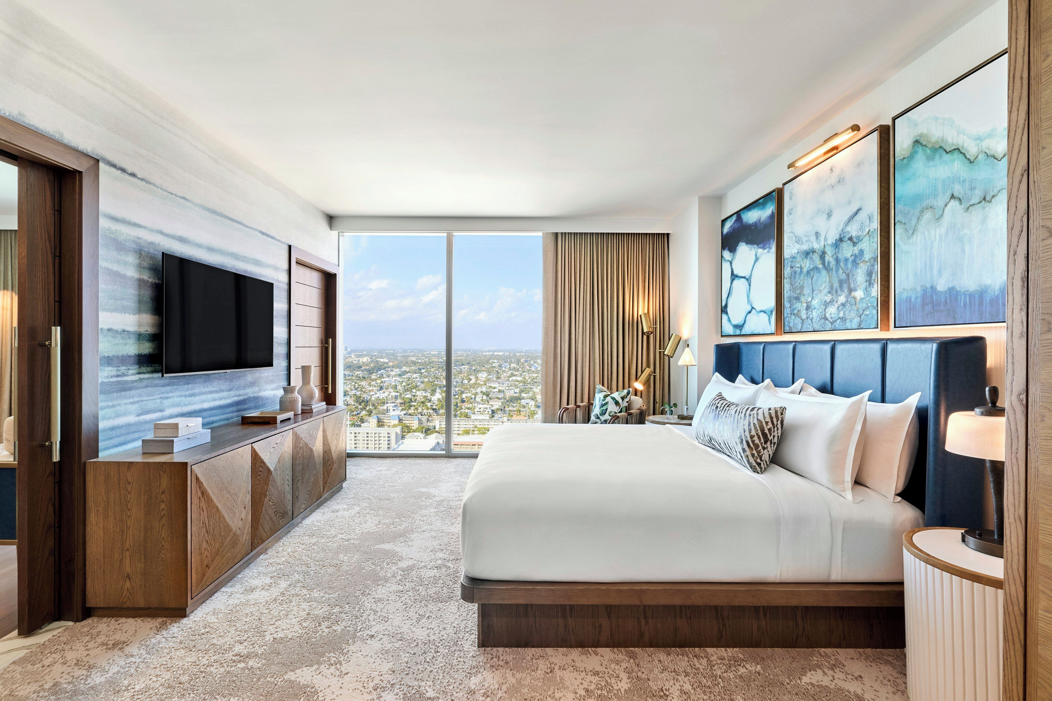 Ein Hotelzimmer mit einem großen Bett, einem Fernseher an der Wand und Blick auf die Stadt.
