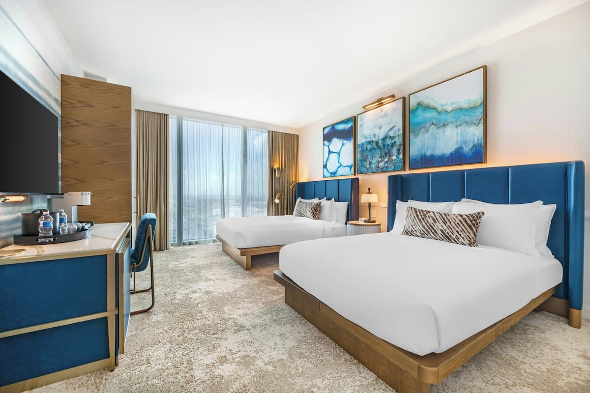 Une chambre d’hôtel avec deux lits, un bureau, une télévision et des œuvres d’art accrochées au mur.