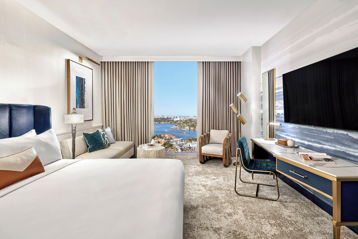 Une chambre d’hôtel comprenant un lit, un bureau, une chaise, un canapé et donnant sur un plan d’eau.