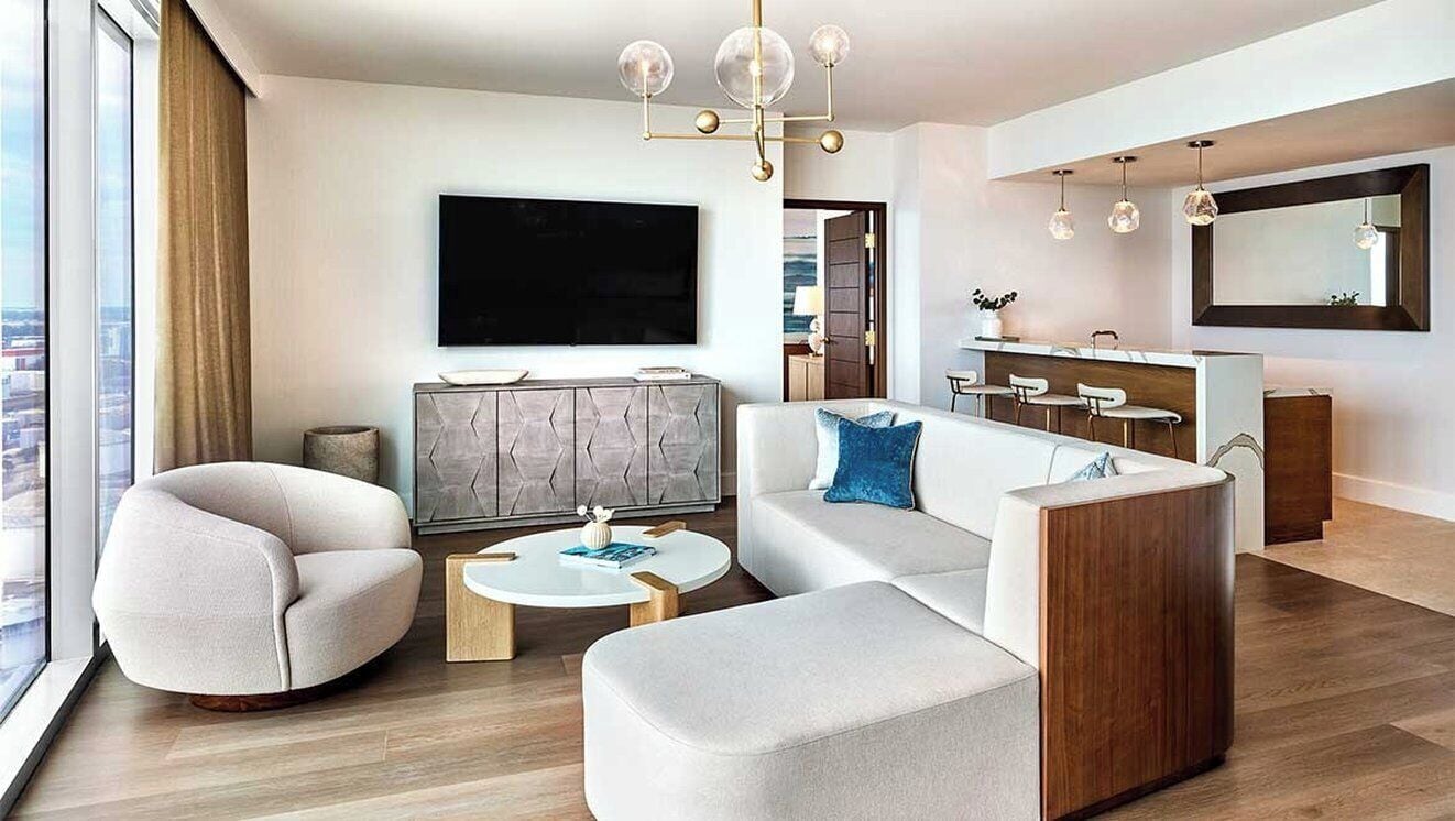 Una sala de estar moderna con sofá, sillón, mesa de centro, televisor y un comedor con sillas.