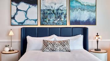 A hotel room with a large bed, two bedside tables, and three abstract paintings on the wall.