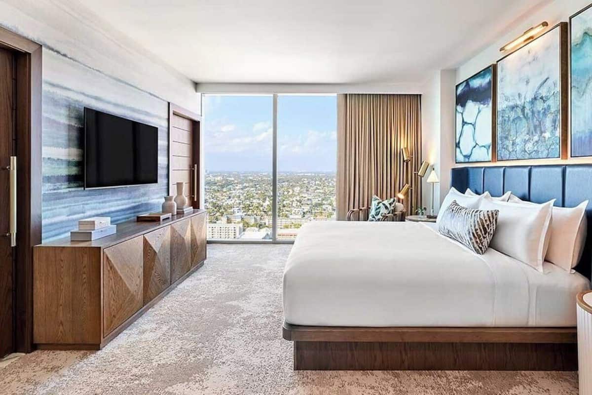 Une chambre d’hôtel moderne avec un grand lit, un téléviseur fixé à un meuble en bois et une vue sur la ville.