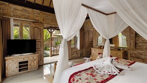 A bedroom with a large bed, a TV, wooden furniture, and a balcony with plants. - Kumala Ubud Villa (Ubud)