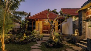 A house with a red-tiled roof, stone walls, and a well-maintained garden with stepping stones and tropical plants. - Kumala Ubud Villa (Ubud)