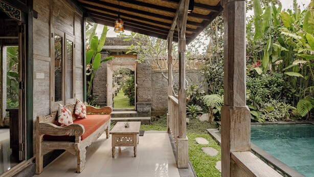 A covered outdoor seating area with a wooden bench and table, a stone pathway, and a pool. - Kumala Ubud Villa (Ubud)