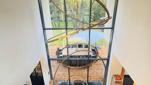 A modern interior with a large window, a wooden dining table, and a unique circular light fixture. - Design house in the heart of the forest Escape & absolute comfort (Roquefort-les-Pins)