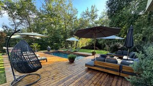 A wooden deck with a hanging chair, a pool, and outdoor seating with umbrellas. - Design house in the heart of the forest Escape & absolute comfort (Roquefort-les-Pins)