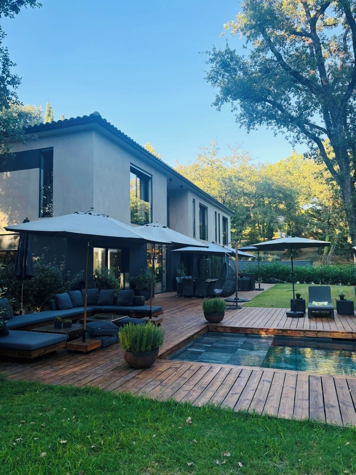 A modern house with a patio area featuring a pool, outdoor seating, and umbrellas.