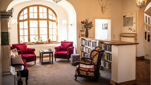 A library with arched windows, red armchairs, a wooden table, and a bookshelf. - Cozy vacation apartment for up to 4 people on the first floor of a manor house (Alt Necheln)