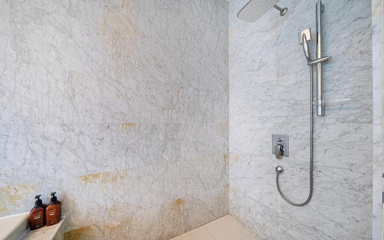 A bathroom with a shower, marble walls, and a sink with two bottles of shampoo.